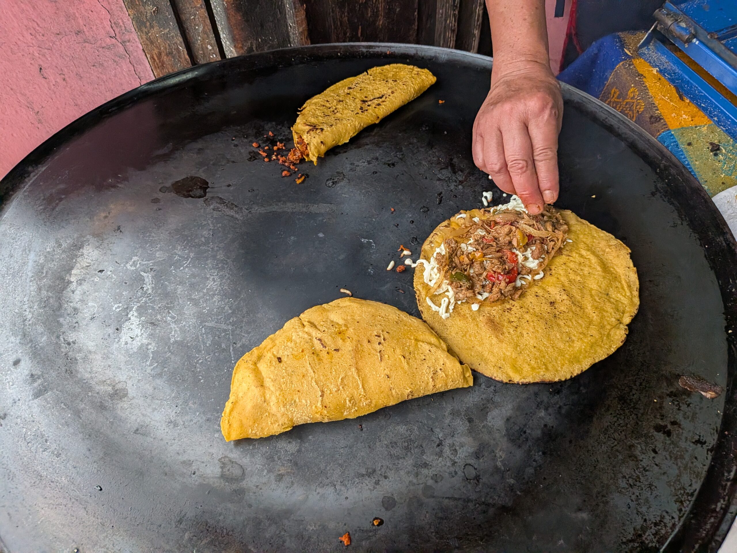 Dely Quesadillas 攤位特寫,廚師正使用大平底鍋烹飪 Quesadillas,展現道地小吃製作過程。