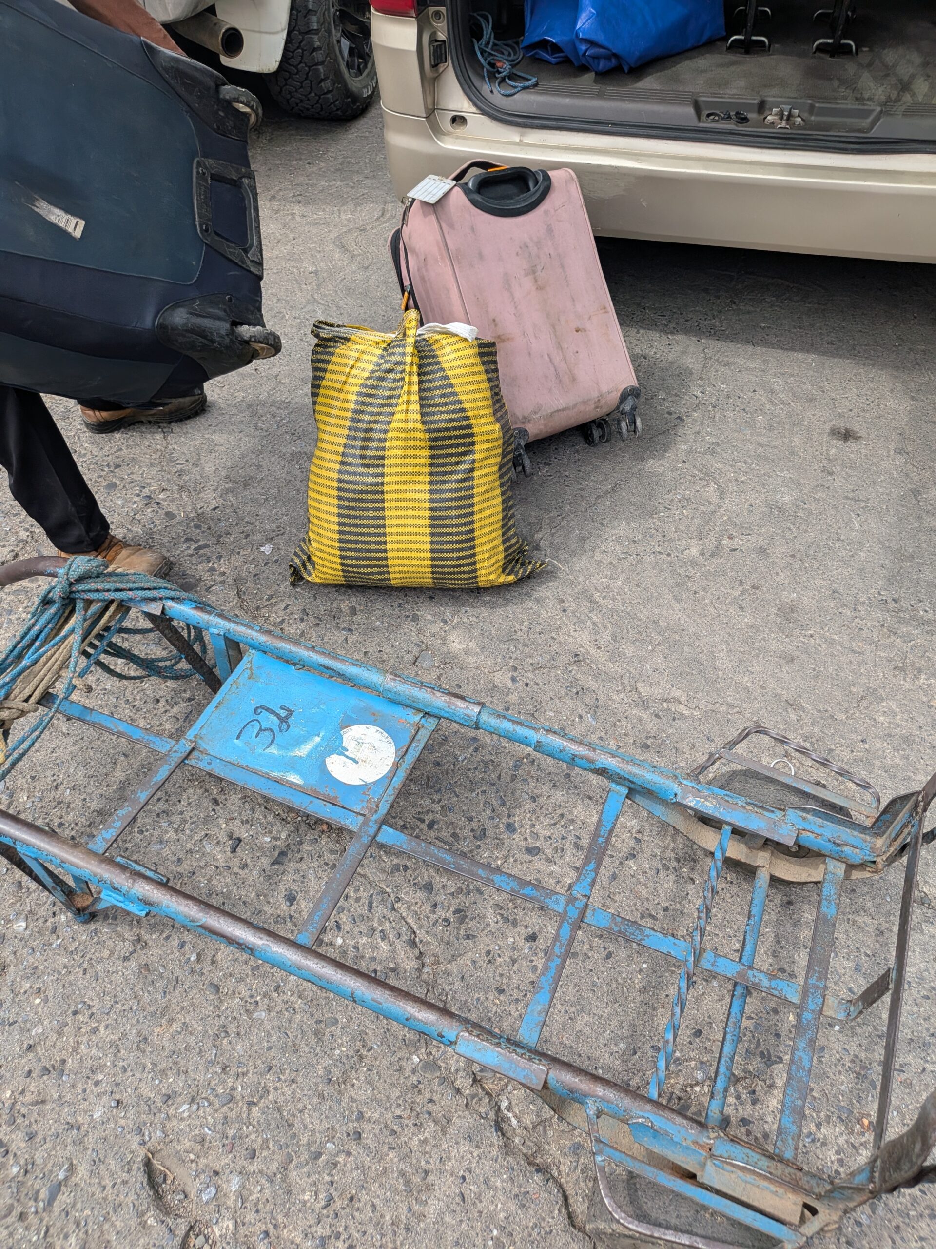 抵達瓜地馬拉與墨西哥邊境時，當地行李工用來協助旅客搬運行李、帶有編號的藍色鐵製推車，一旁可見旅客的大型行李與跨國接駁車。